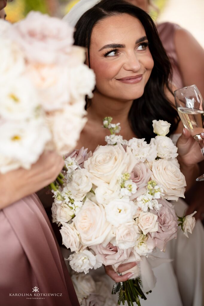 Smiling bride holding a pastel rose bouquet with champagne glass, designed by Paperwhite Floral Design at Achnagairn Castle wedding.
